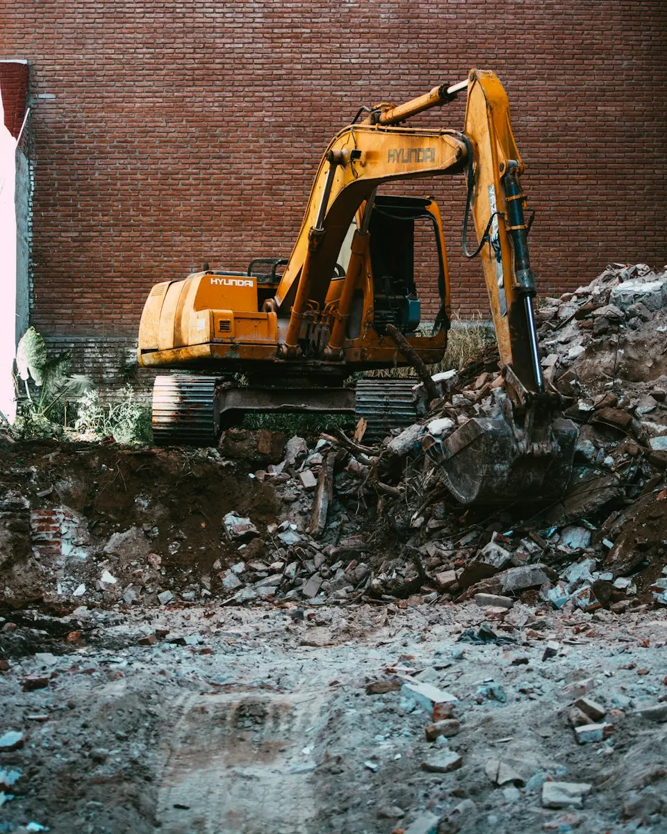 Orangefarbener Bagger auf Bauschutt vor einer Backsteinwand