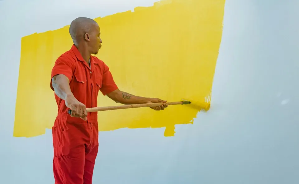 Mann streicht eine Wand mit gelber Farbe